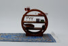 A miniature circular wooden shelf with three tiers, styled with tiny books, wine glasses, a teacup, and a miniature rug on a white studio background.