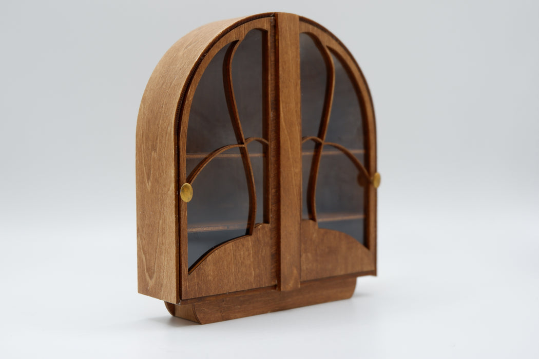 1:12 scale wooden miniature of an arch-topped display cabinet. It has 2 doors with clear plastic windows that hinge open from the center. Each door has a gold-colored oval knob.